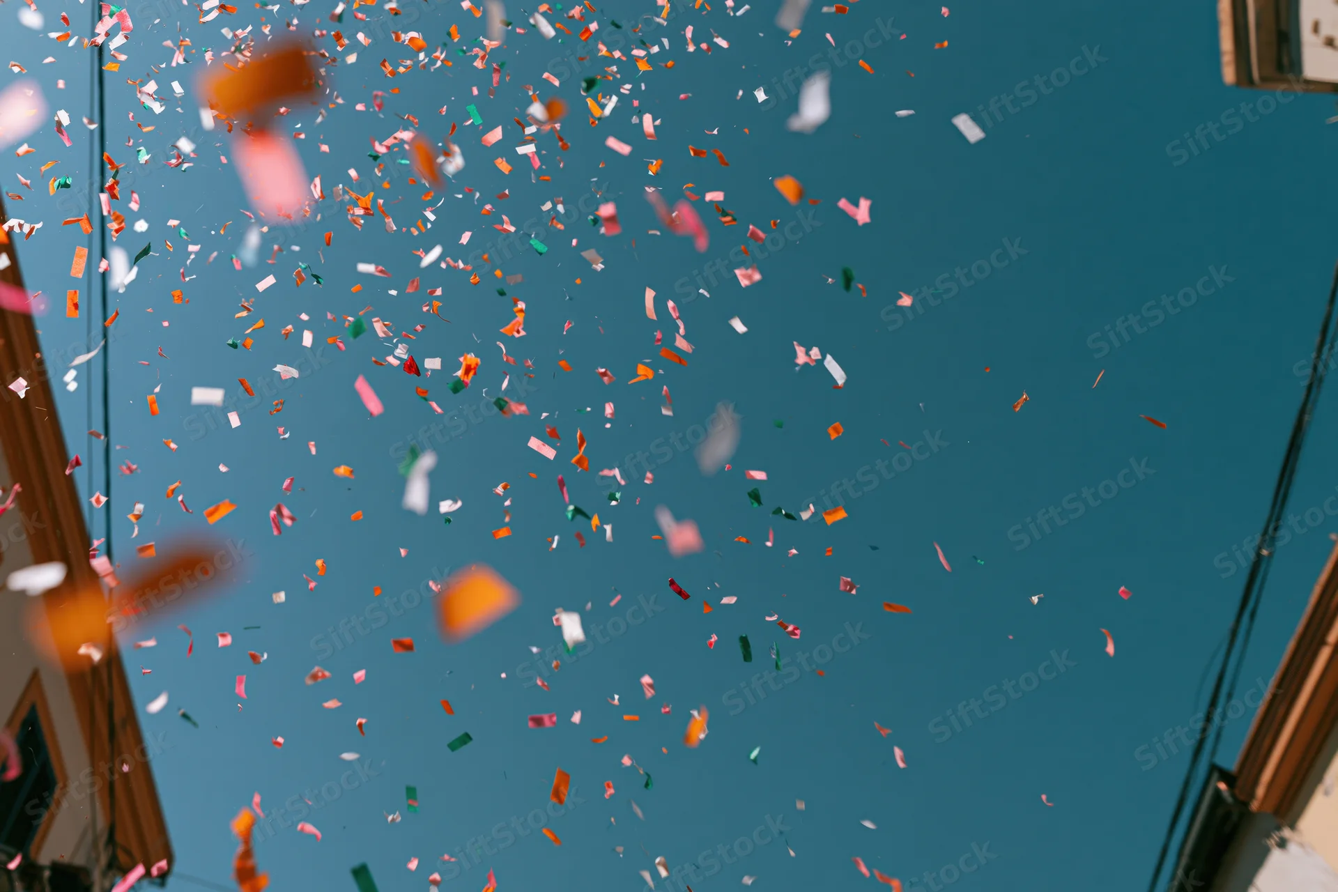 Colorful confetti floating upward in a clear blue sky above a narrow urban street