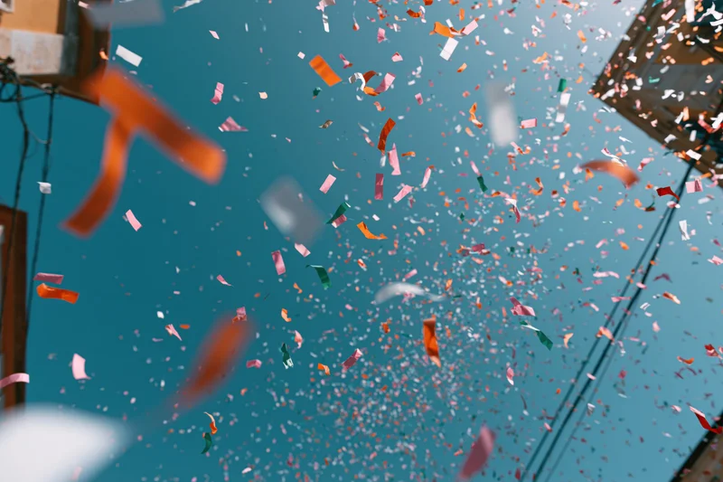 Colorful confetti flying upward against a clear blue sky between buildings