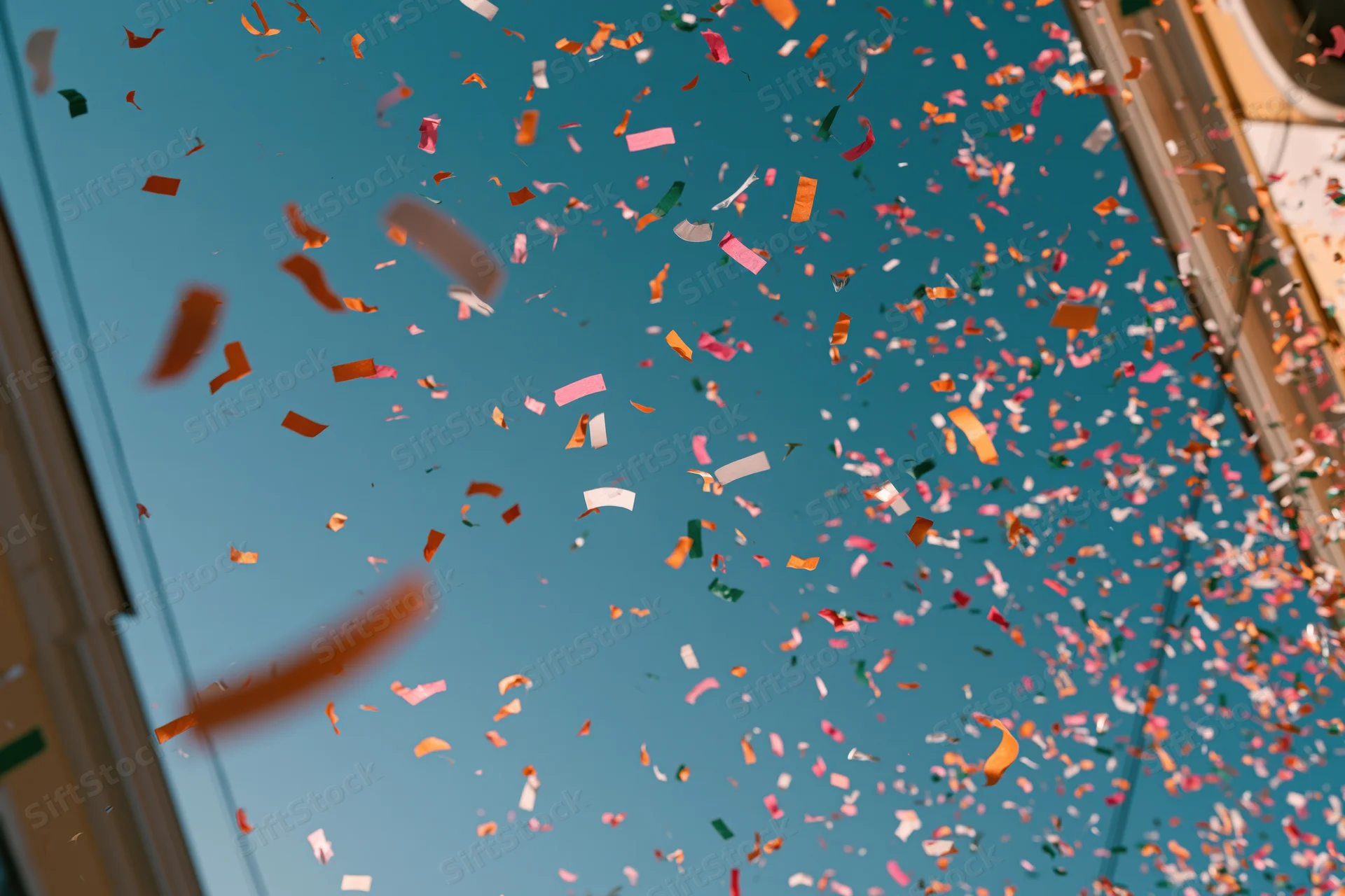 Colorful confetti floating upward against a clear blue sky viewed through a window frame