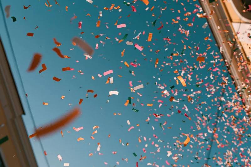 Colorful confetti floating upward against a clear blue sky viewed through a window frame