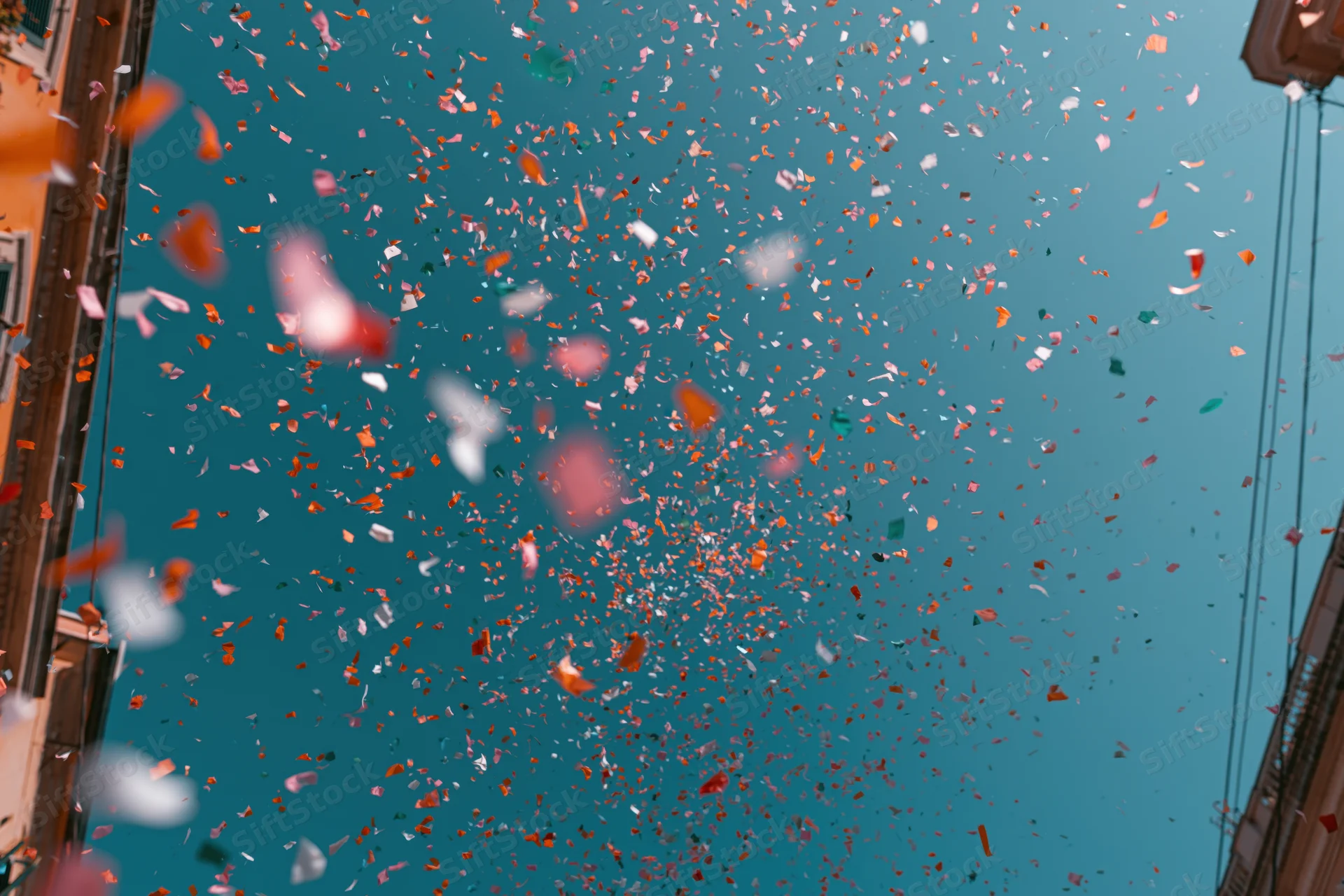 Colorful confetti floating upward in a city street against a clear blue sky