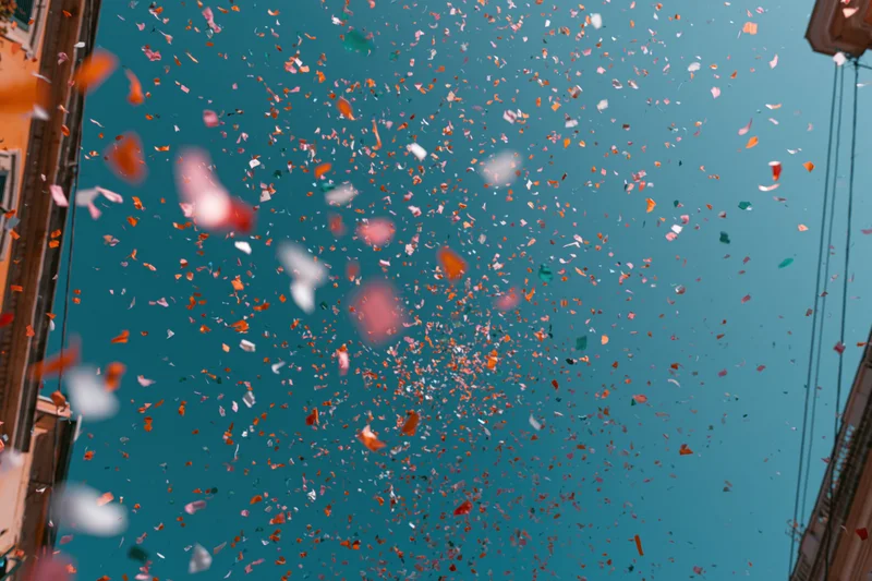 Colorful confetti floating upward in a city street against a clear blue sky