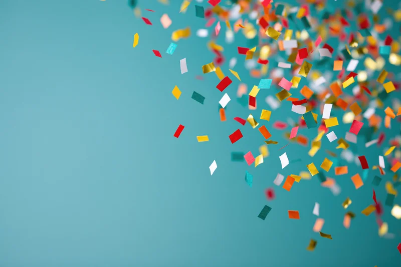 Colorful paper confetti pieces falling mid-air against a teal background with copyspace on the left
