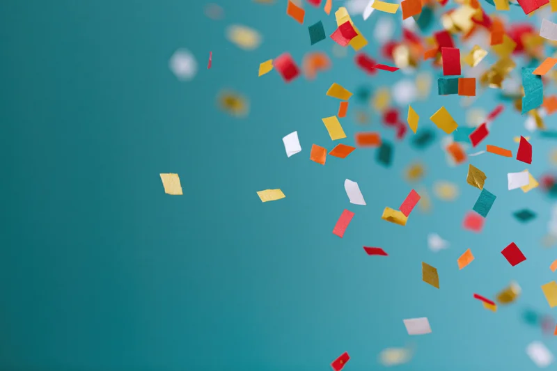 Colorful paper confetti pieces falling across teal background with copyspace on left