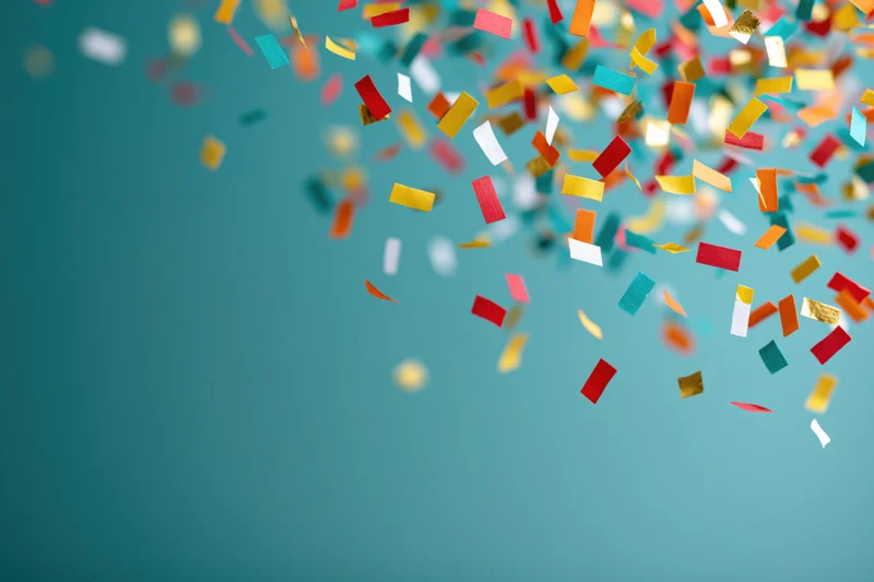 Colorful paper confetti pieces falling across a teal background with copyspace on the left