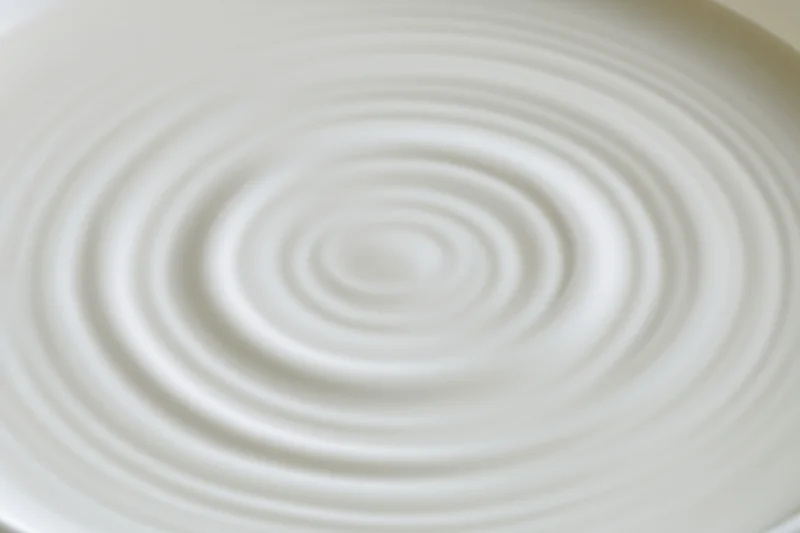 Concentric ripples spreading across the surface of white milk in a bowl