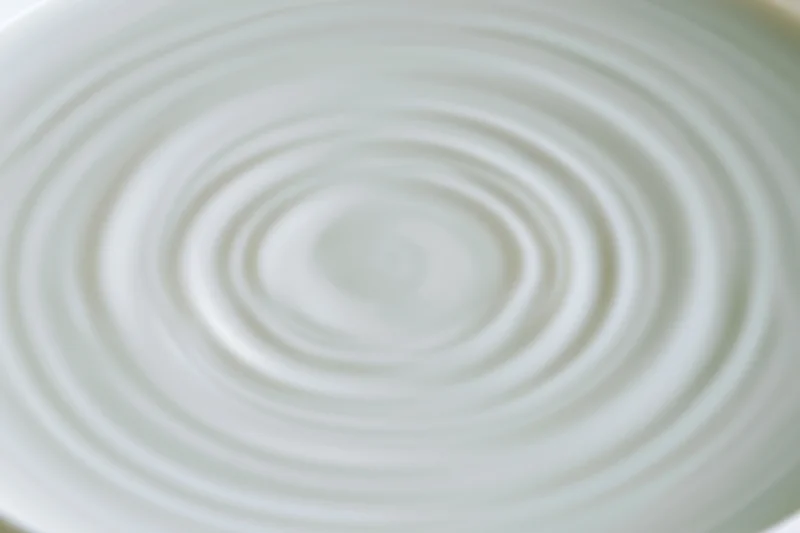 Concentric ripples spreading across the surface of white milk in a bowl
