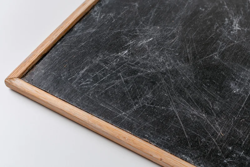 Corner of a worn chalkboard with white scratches and wooden frame on white background