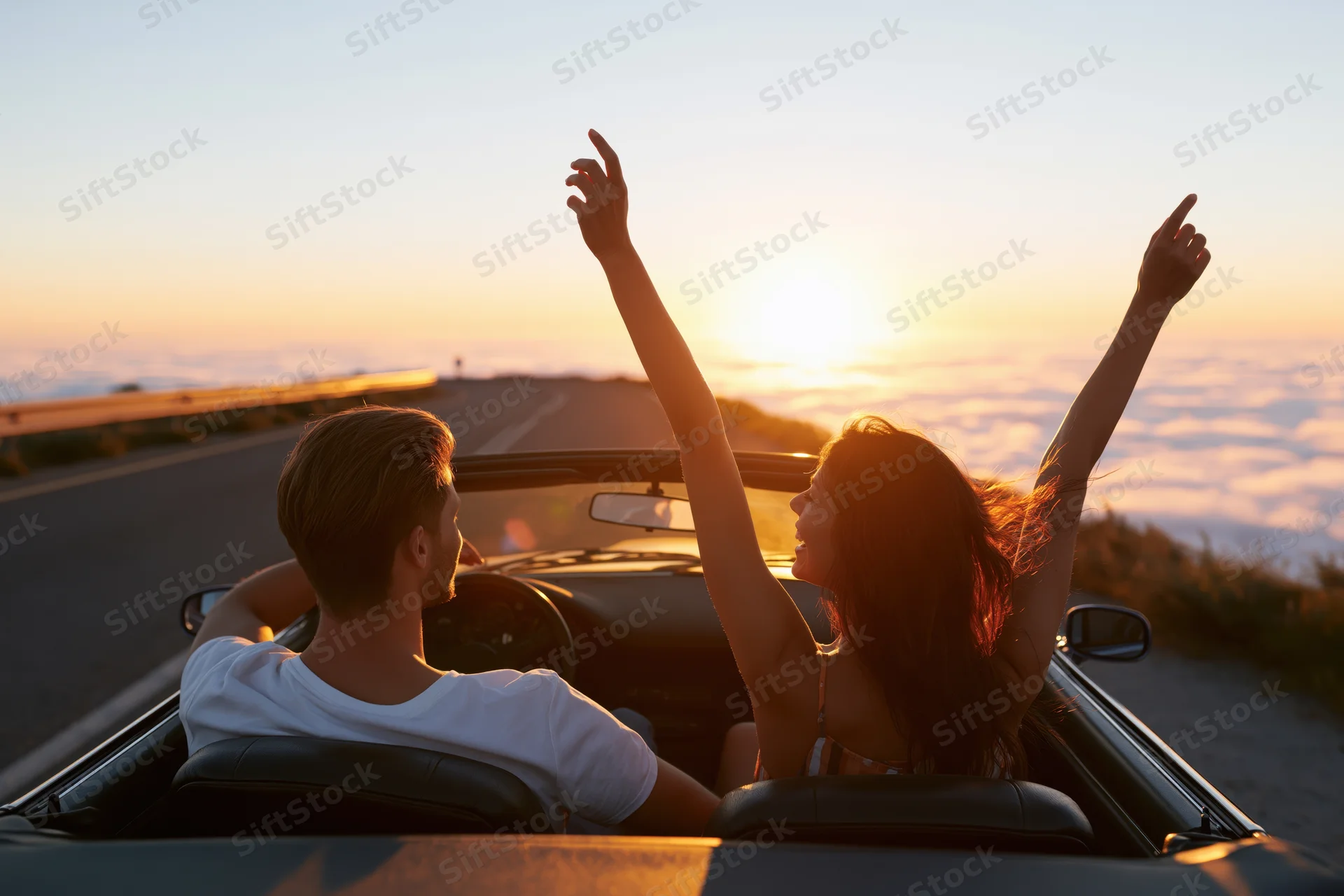 Couple driving a classic convertible on a winding mountain road at sunset
