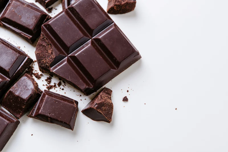 Dark chocolate bar broken into pieces on white surface with copyspace