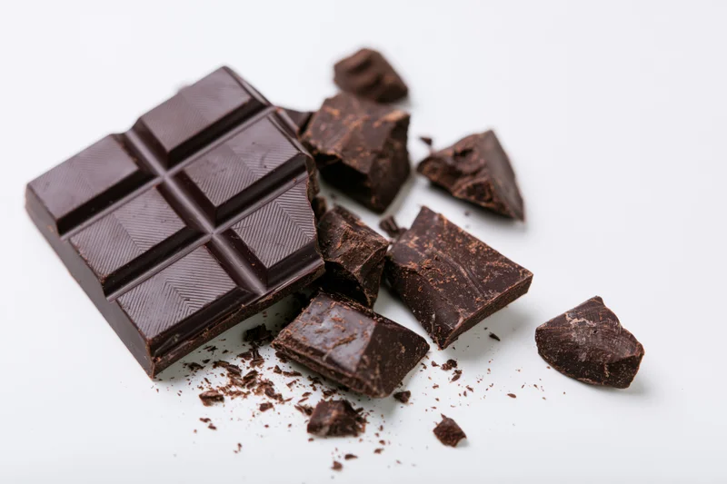 Dark chocolate bar broken into pieces on white background