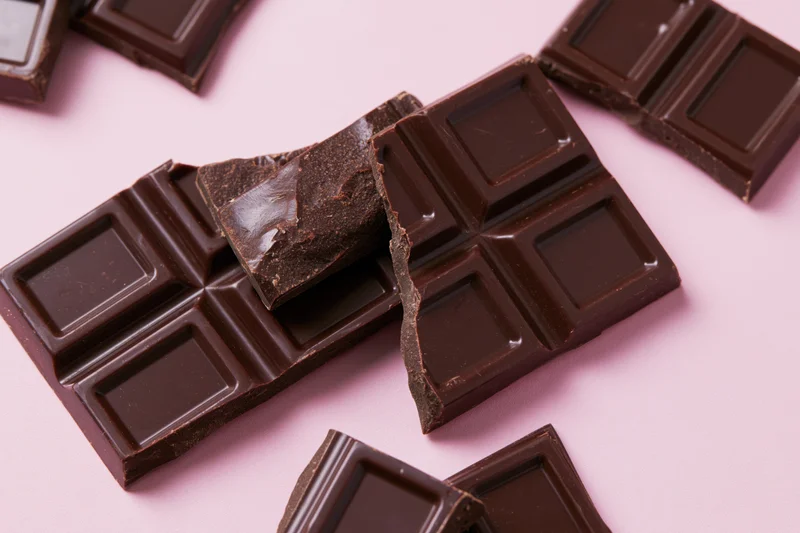 Broken dark chocolate bar pieces arranged on pink background in flat lay view
