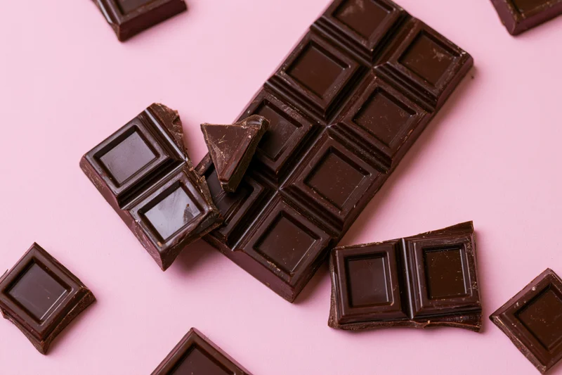 Dark chocolate bar broken into pieces arranged on pink background