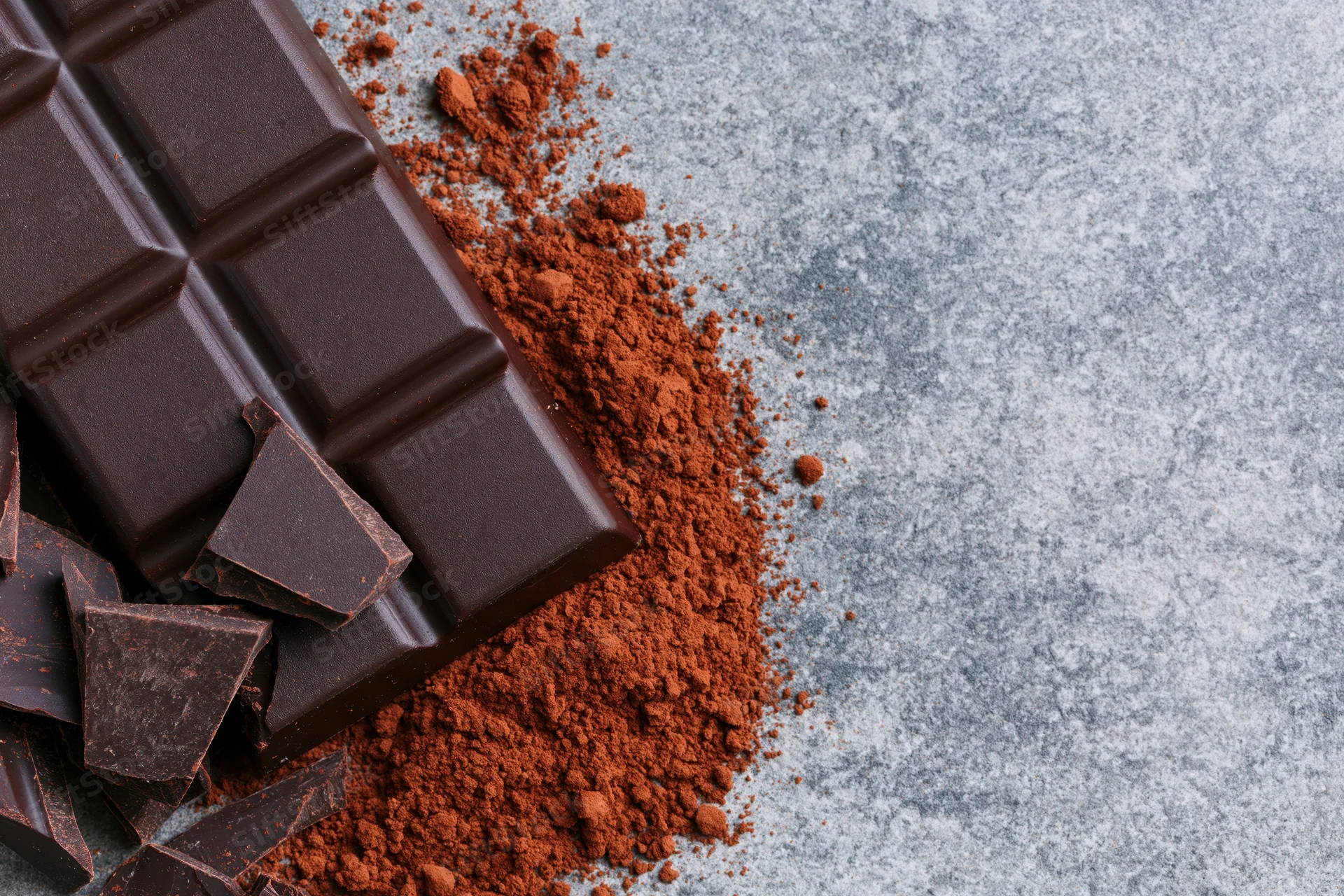 Dark chocolate bar with broken pieces and cocoa powder scattered on a gray stone surface