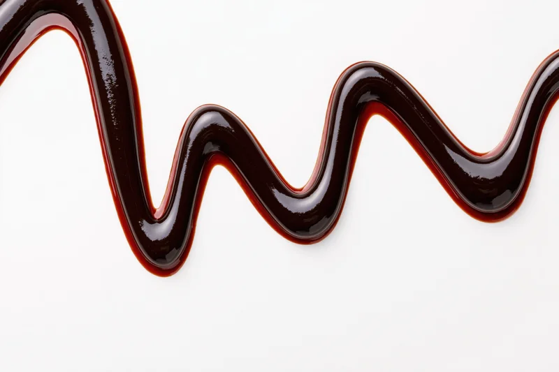 Dark chocolate sauce drizzled in a flowing zigzag pattern on white background