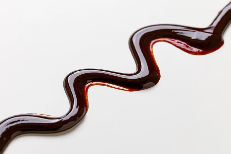 Dark chocolate sauce drizzled in a zigzag swirl on a white surface