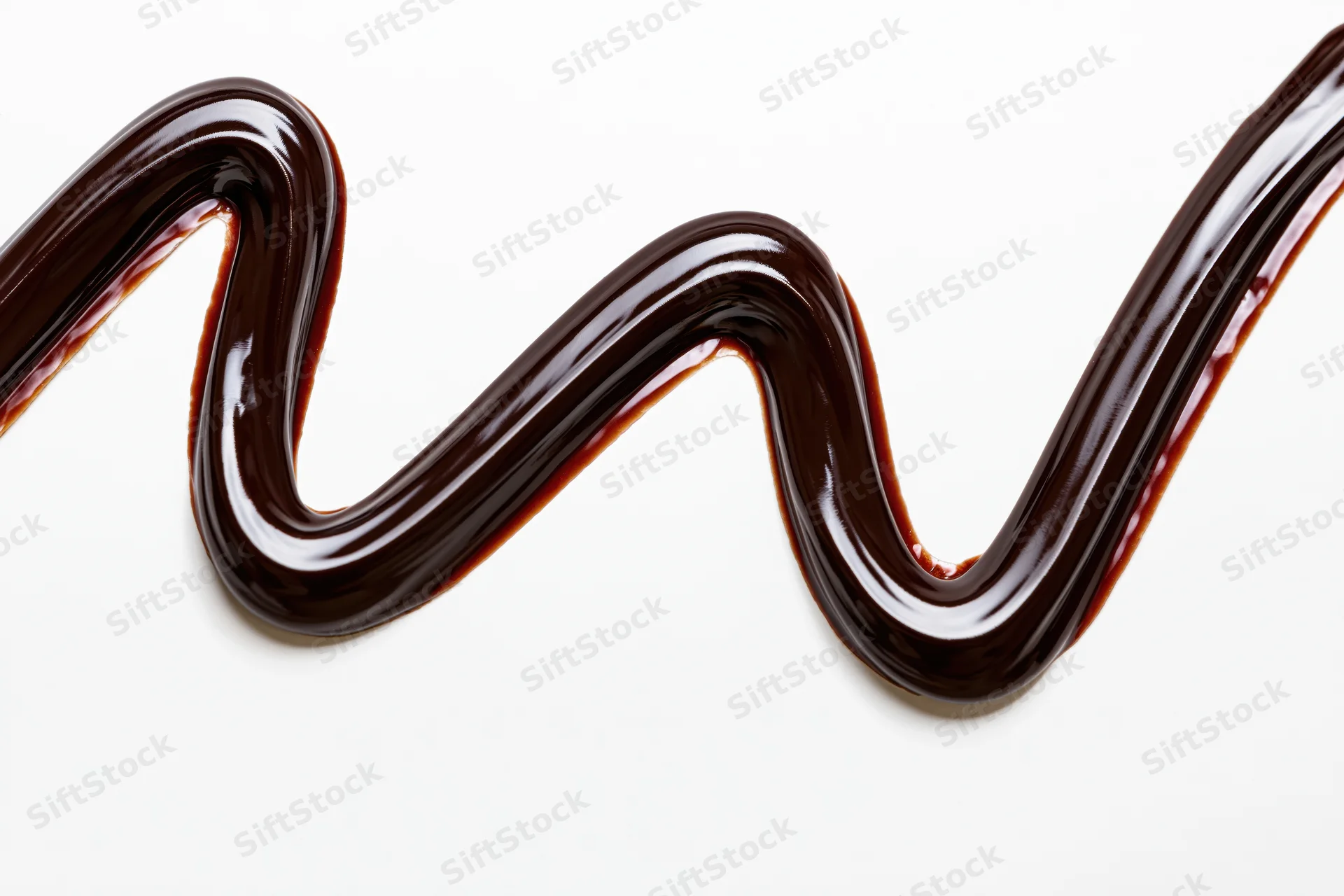 Dark chocolate sauce drizzled in a flowing zigzag swirl on white background