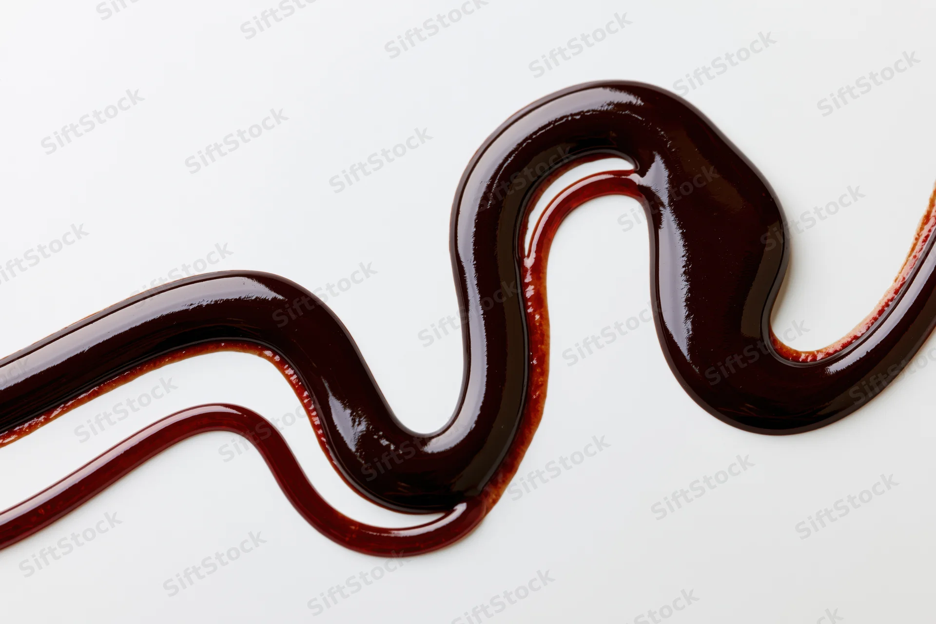 Dark chocolate sauce drizzled in a flowing zigzag swirl on white background