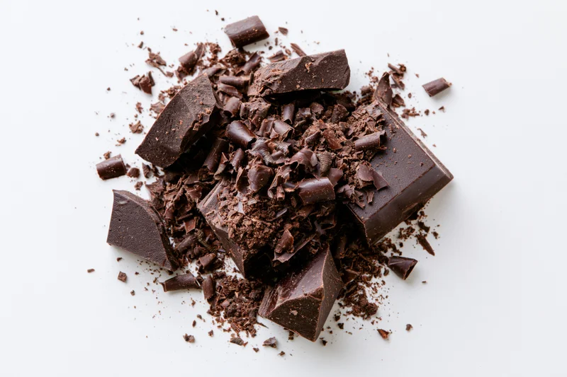 Broken dark chocolate chunks and shavings scattered on white background