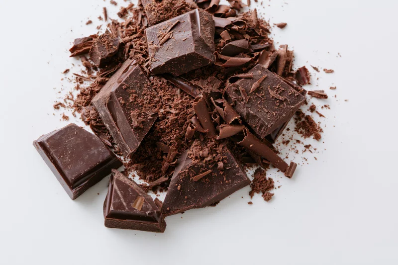 Broken dark chocolate chunks and shavings scattered on white background