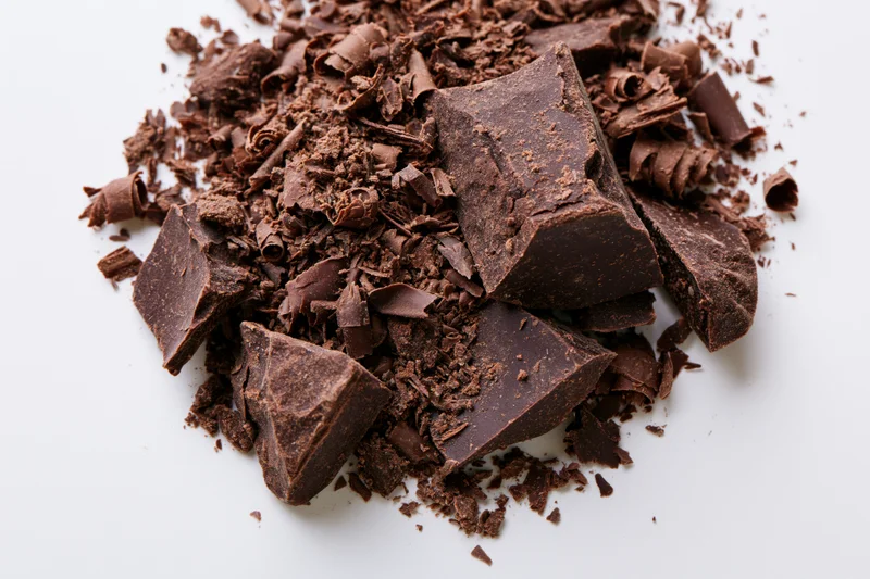 Dark chocolate shavings and broken chunks scattered on white background