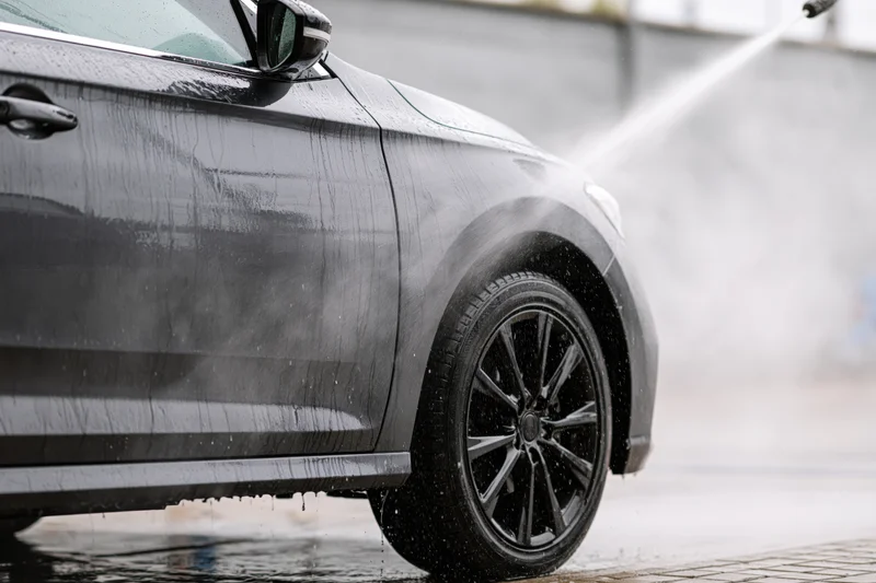 Dark grey sedan being pressure washed at a self-serve car wash