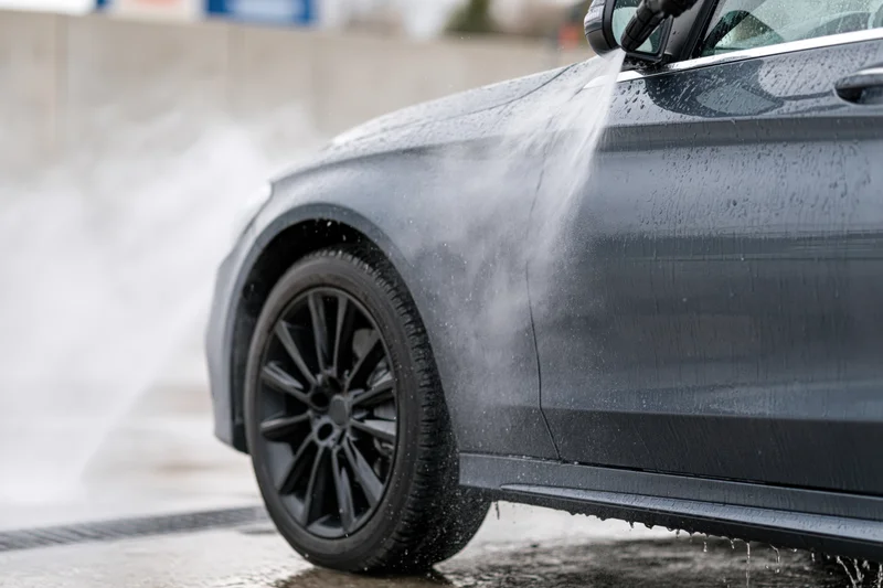Dark grey sedan being pressure washed at a self-serve car wash