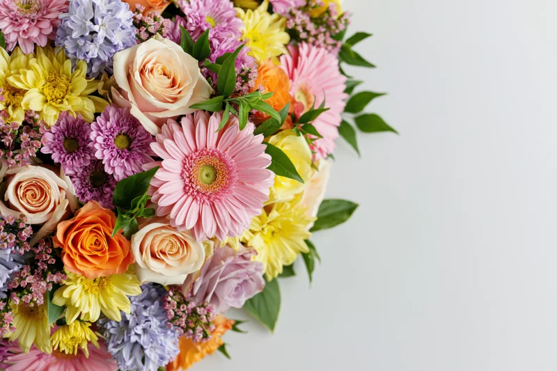 Dense mixed flower arrangement clustered along the left edge with copyspace on white background