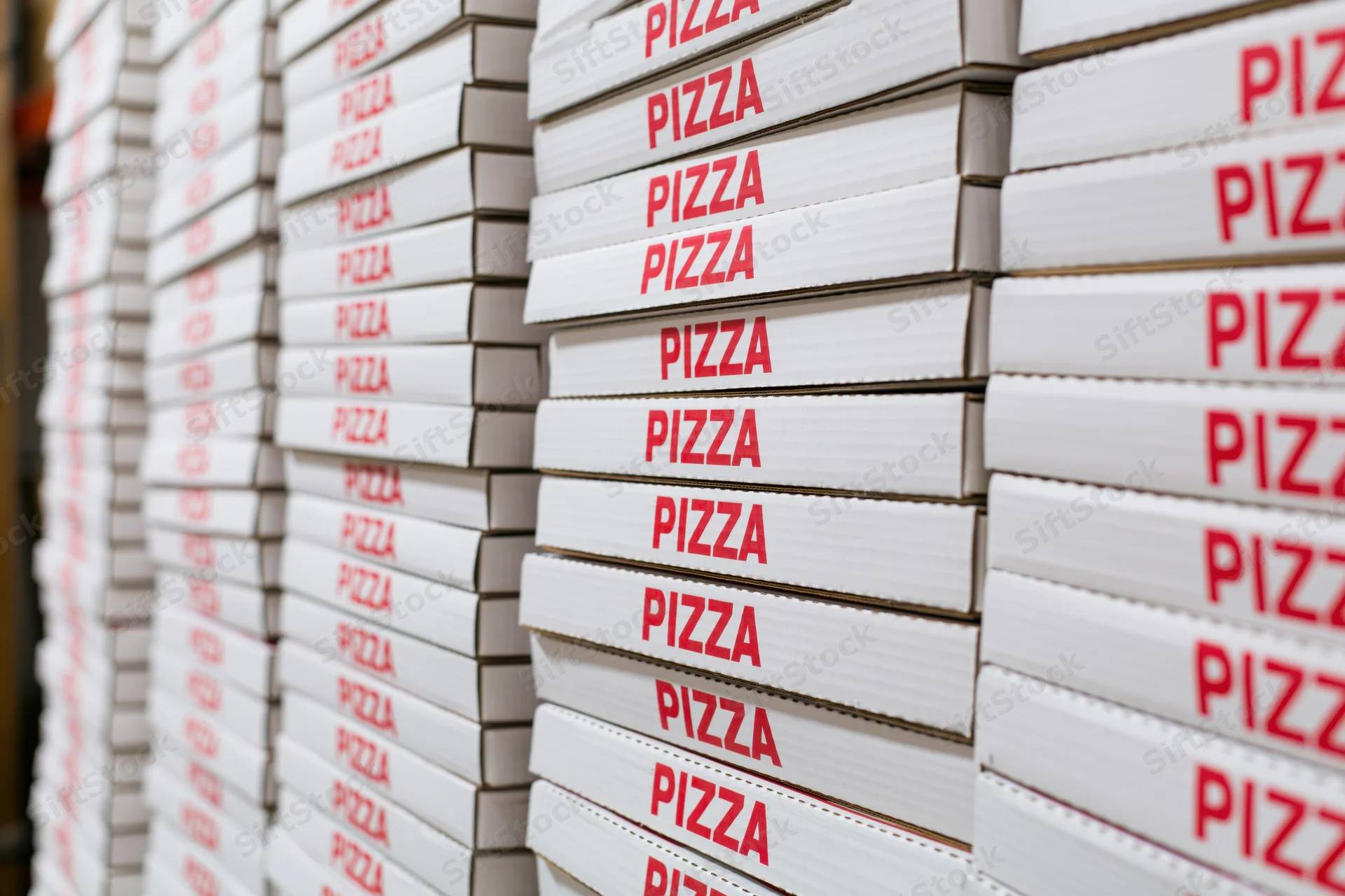 Stacks of white cardboard pizza boxes with red text arranged in rows in a storage area