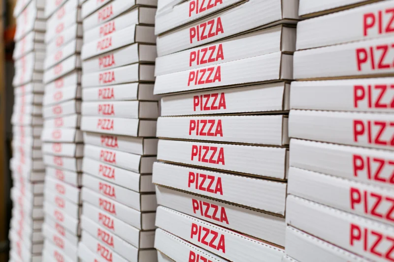 Stacks of white cardboard pizza boxes with red text arranged in rows in a storage area