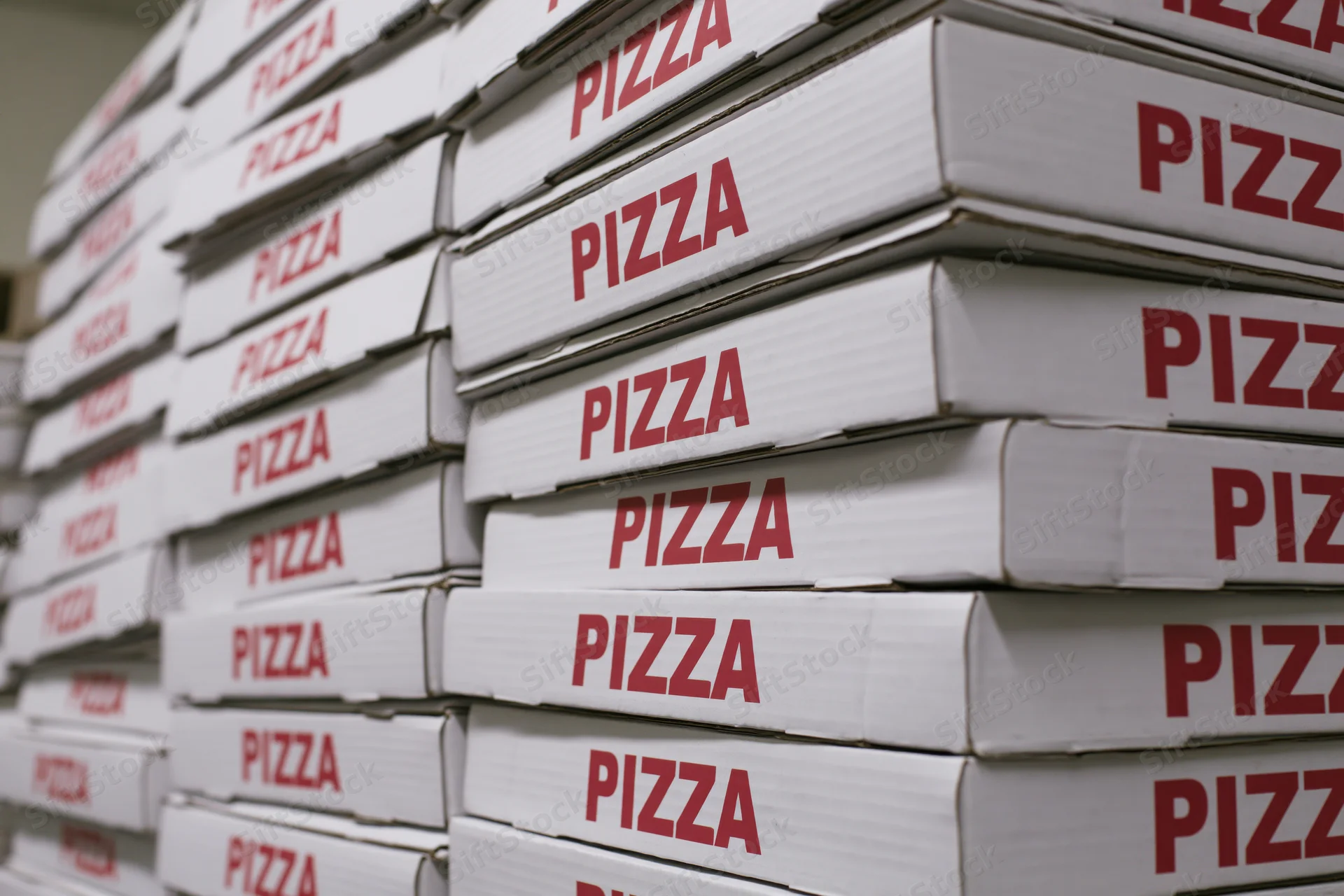 Stacks of white cardboard pizza boxes with red text arranged in rows for delivery or storage