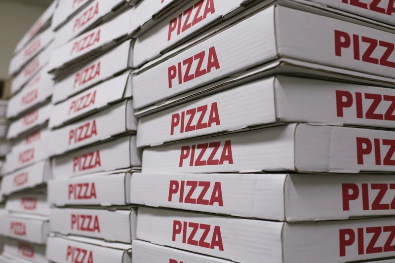 Stacks of white cardboard pizza boxes with red text arranged in rows for delivery or storage
