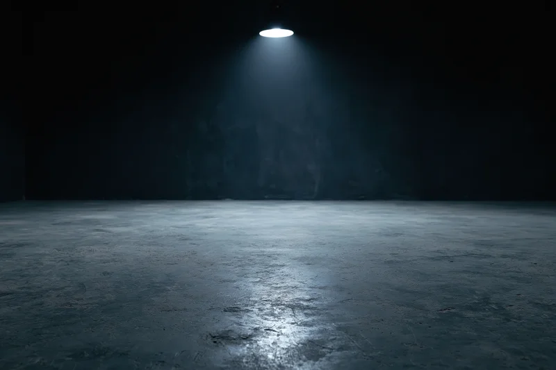 Spotlight illuminating rough concrete floor in dark empty studio interior