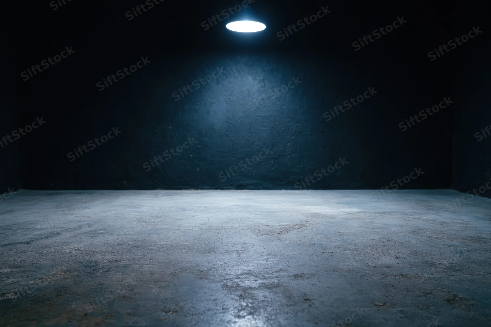 Empty dark studio interior with rough concrete floor and single overhead spotlight