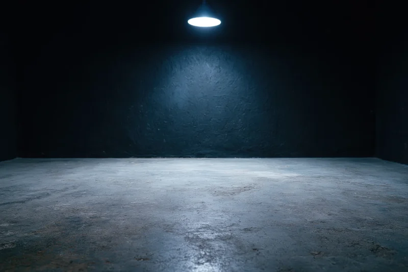 Empty dark studio interior with rough concrete floor and single overhead spotlight