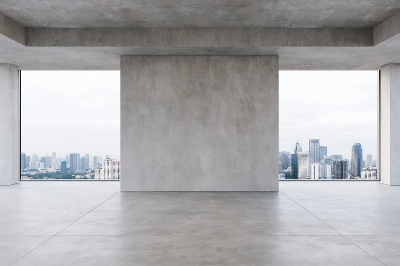 Empty raw concrete room with large freestanding wall and city view through windows