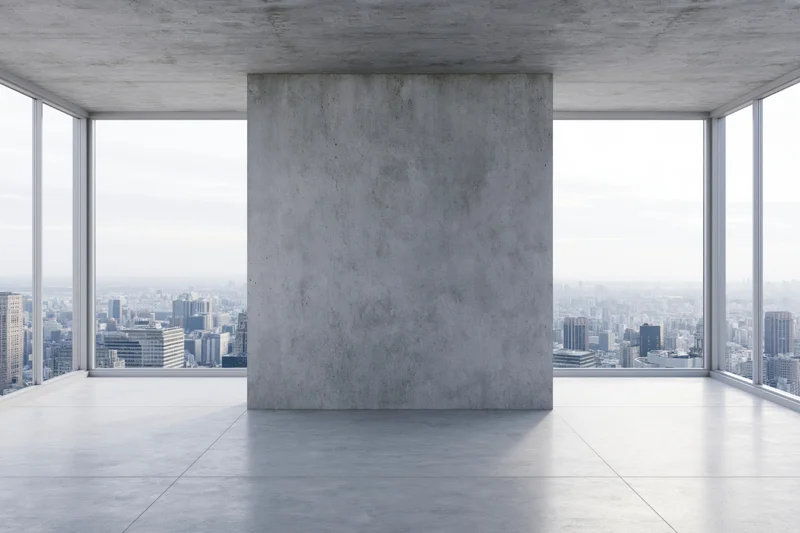 Empty concrete room with large freestanding wall and city view through floor-to-ceiling windows