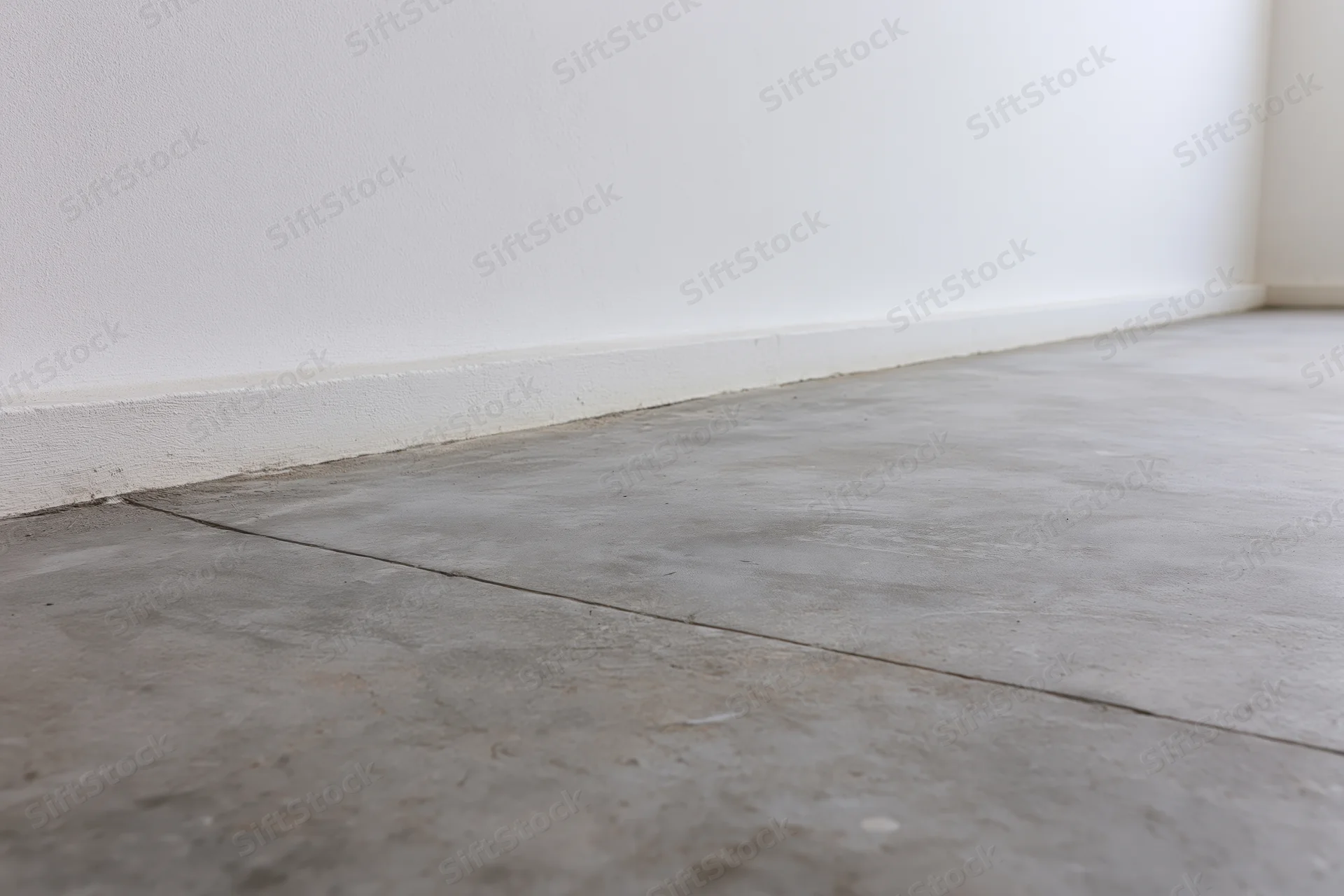 Bare concrete floor meeting smooth white wall in empty room corner