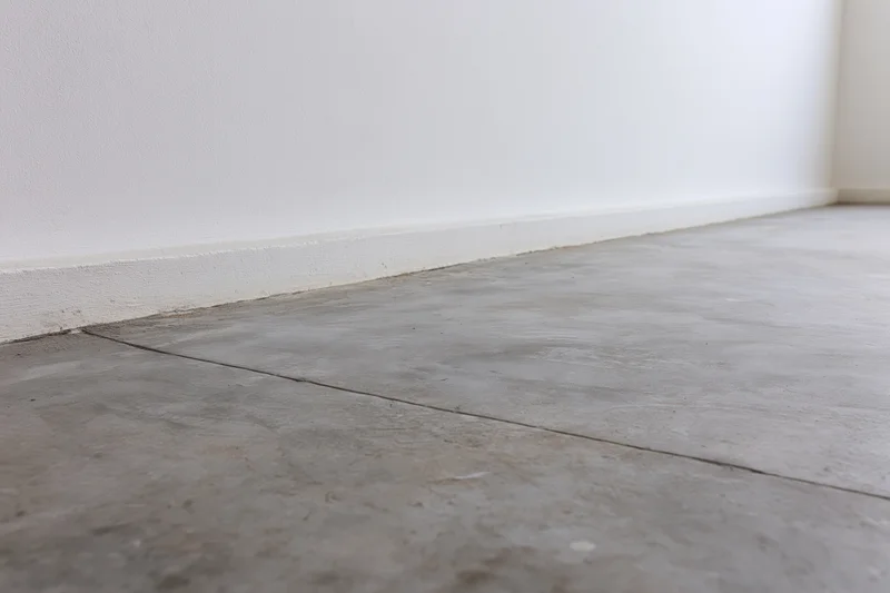 Bare concrete floor meeting smooth white wall in empty room corner