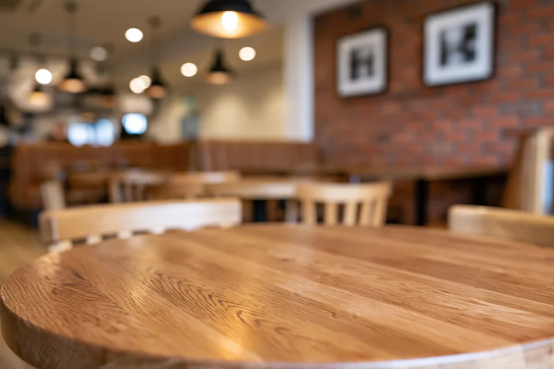 Round wooden table in sharp focus with blurred restaurant interior in background