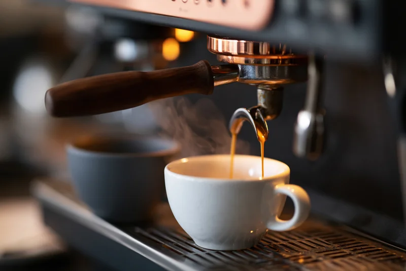 Espresso pouring from a professional coffee machine portafilter into a white cup on a drip tray