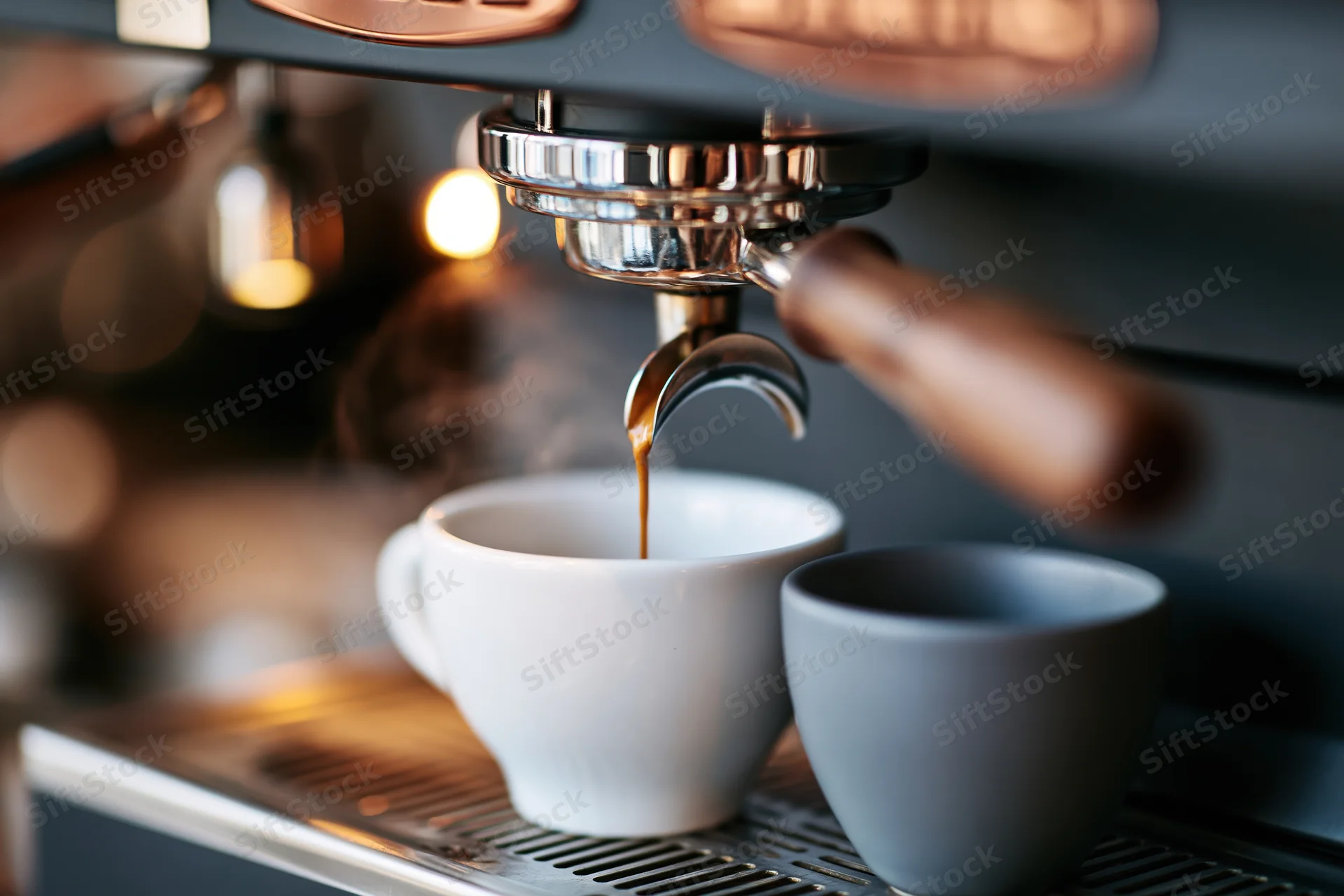 Espresso pouring from a professional coffee machine portafilter into a white cup on a drip tray