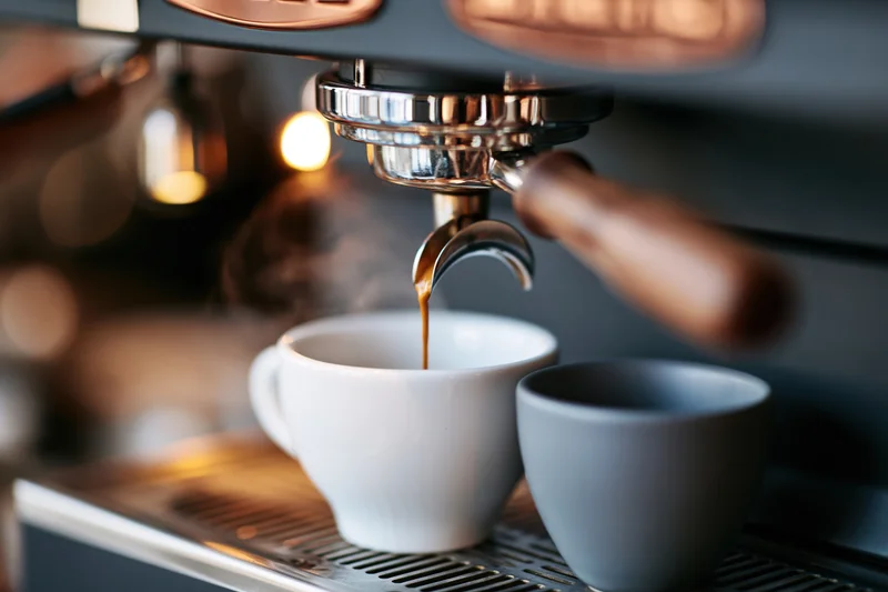 Espresso pouring from a professional coffee machine portafilter into a white cup on a drip tray