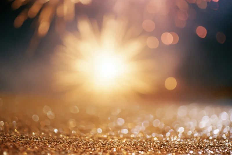 Fireworks bursting in the night sky above a glittering golden surface