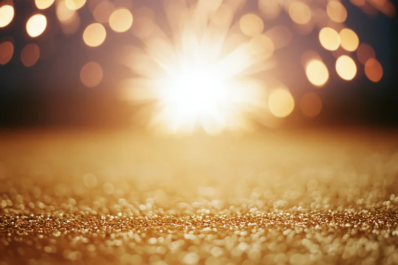 Fireworks bursting in the night sky above a glittering golden surface