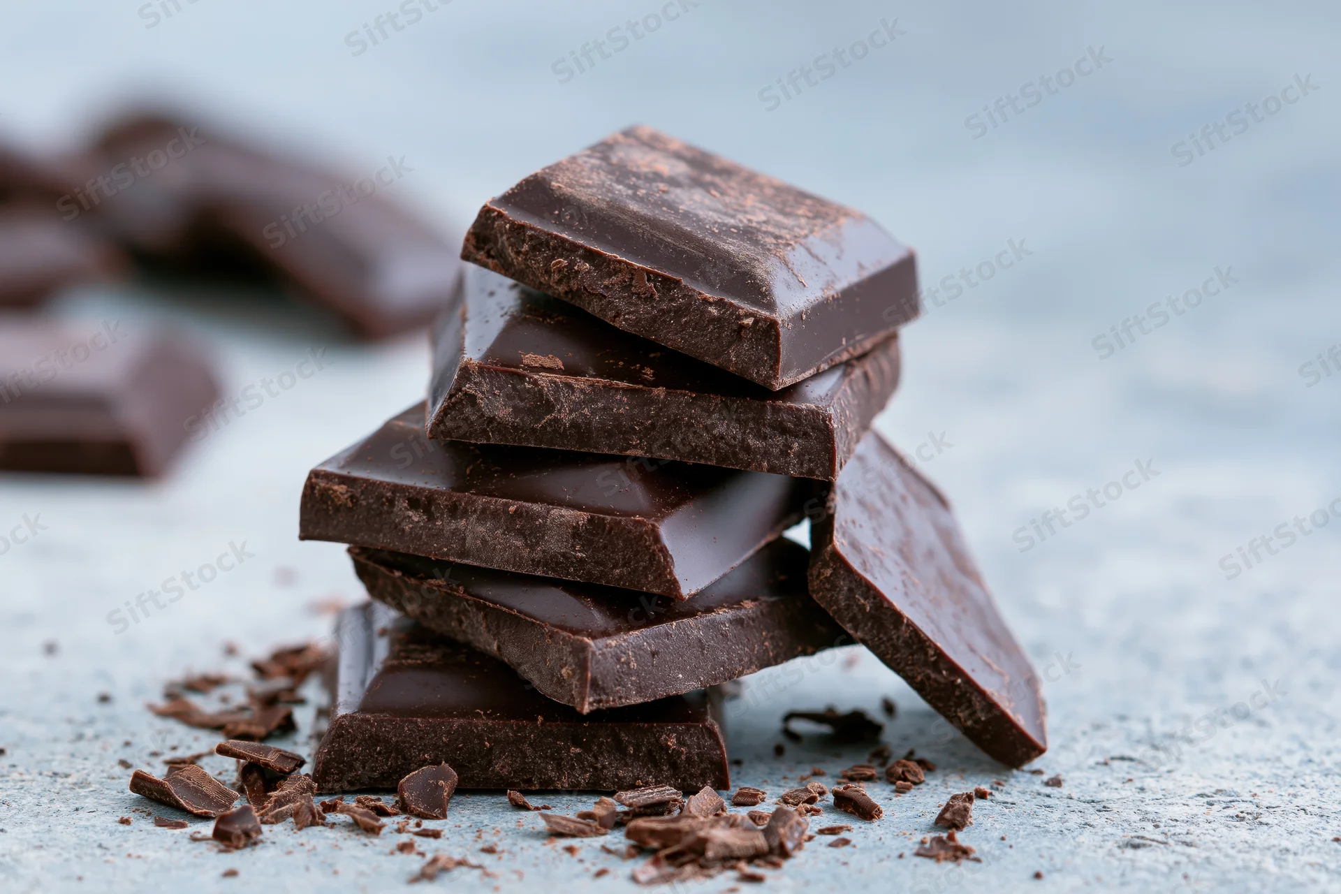 Broken dark chocolate squares stacked unevenly on a light surface with crumbs scattered around