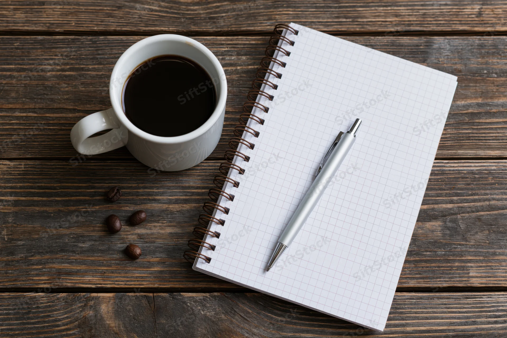 White ceramic mug with black coffee beside a spiral notebook and pen on a wooden table