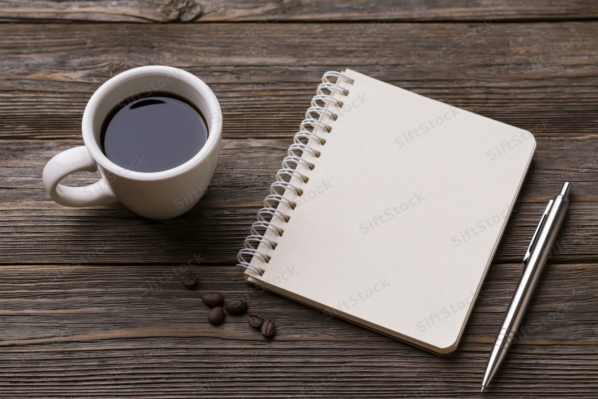 White ceramic mug with black coffee, spiral notebook and pen arranged on dark wooden table