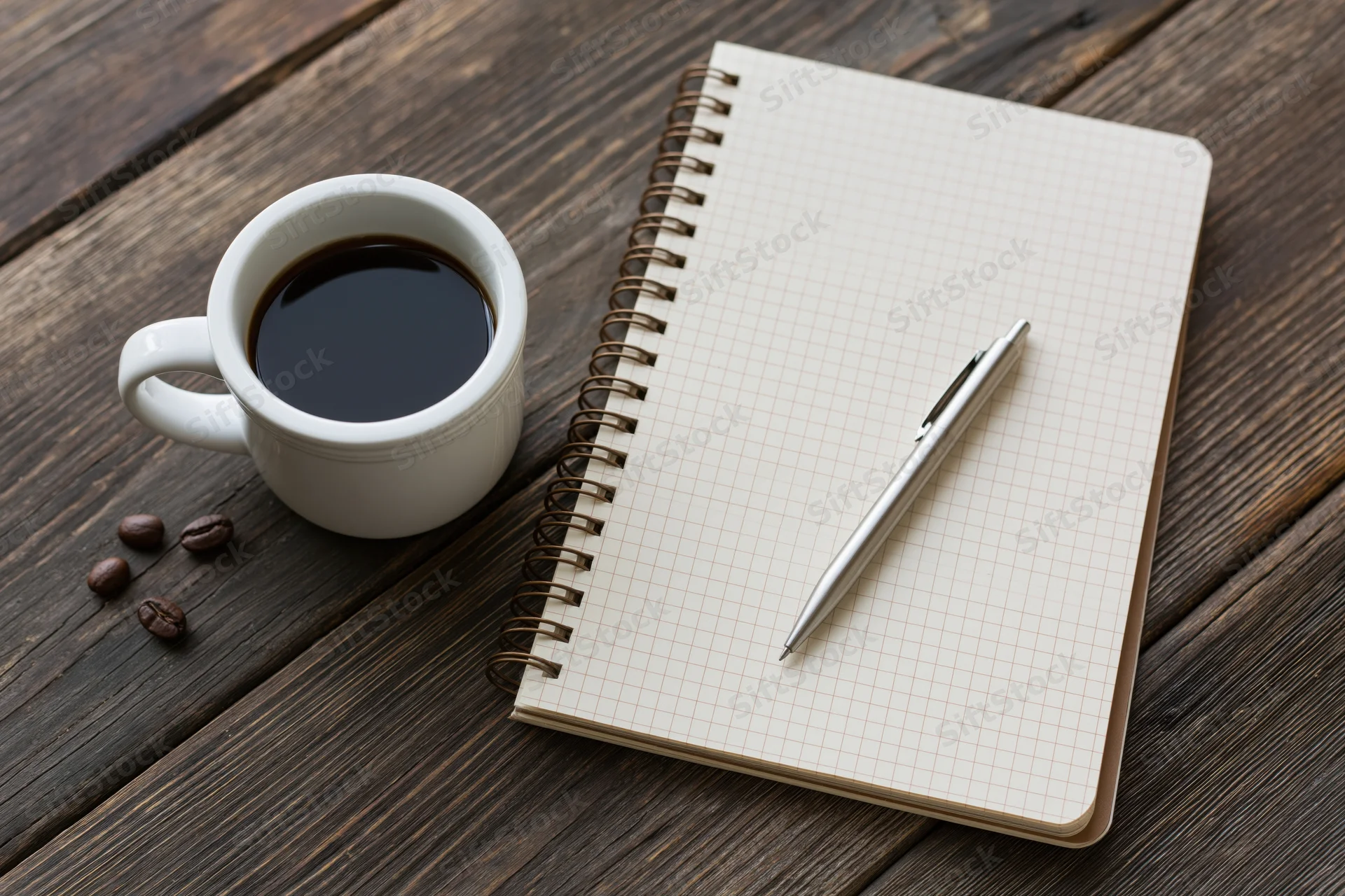 White ceramic mug with black coffee beside a spiral notebook and pen on a wooden table
