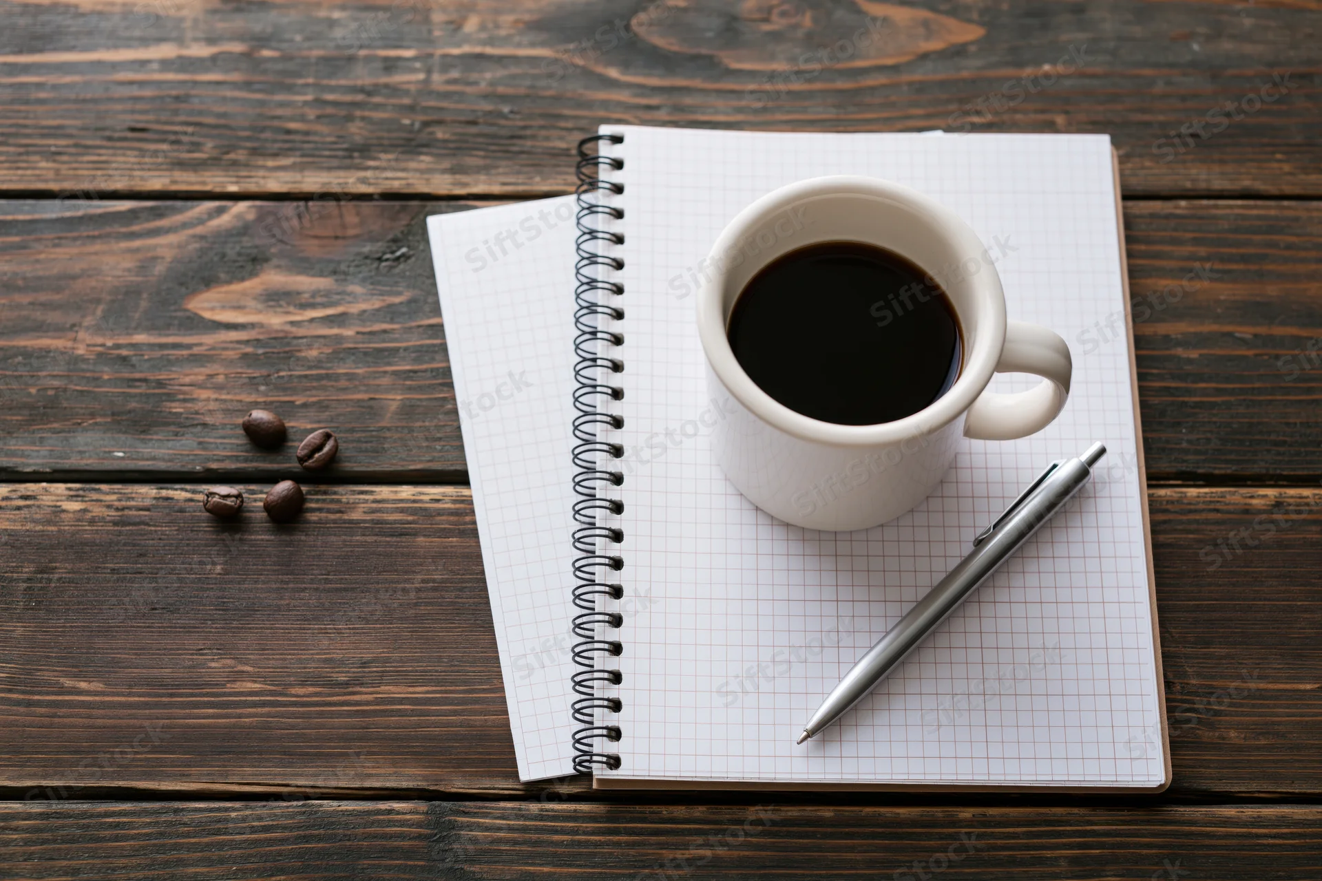 White ceramic mug with black coffee on a grid notebook beside a pen on dark wooden table